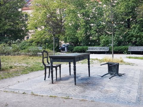 Denkmal "Der geschlossene Raum" auf dem Koppenplatz: Ein Tisch. Zwei Stühle. Ein Stuhl liegt auf der Rückenlehne.