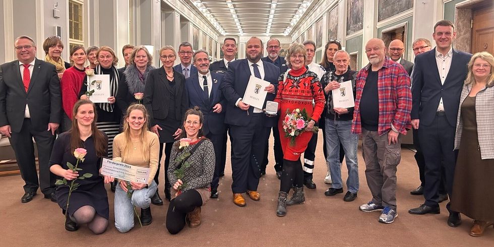 Eine Gruppe Menschen steht zusammen in einer Halle. Vielen halten Blumen oder Urkunden in der Hand.