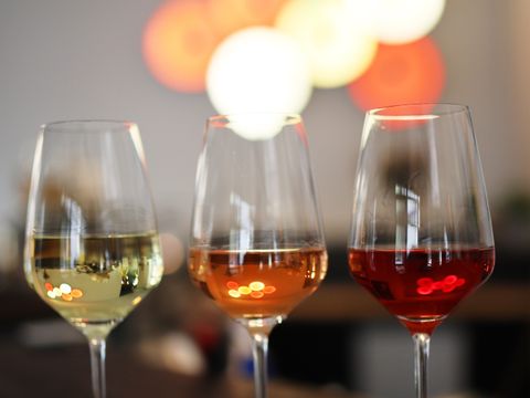 Drei Weingläser stehen auf einem dunklen Tresen. Das linke ist zur Hälfte gefüllt mit Weiswein, das mittlere mit Roséwein und das rechte Glas mit Rotwein