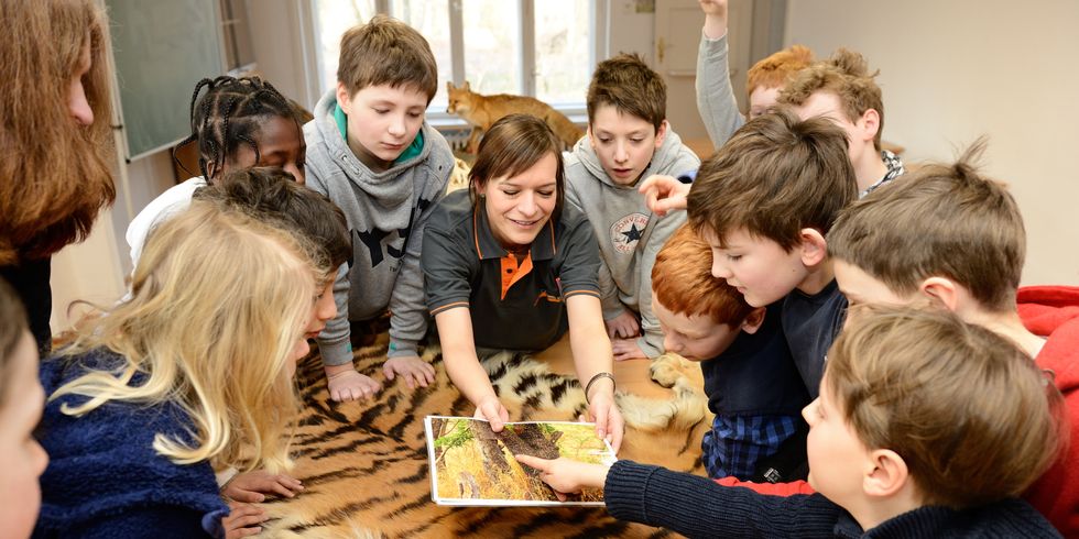 Gruppe von Kindern zusammen mit einer Erwachsenen stehen um einen Tisch und agieren miteinander