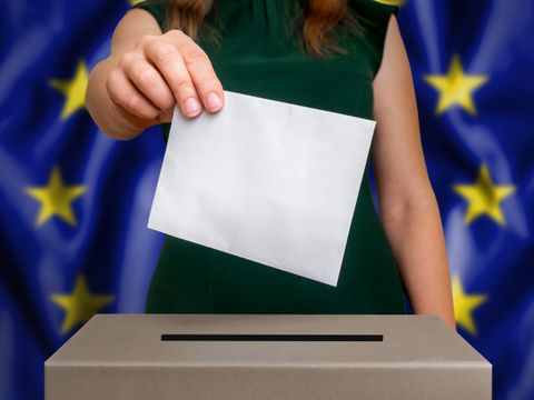 Vor EU-Flagge: Frau steckt einen Umschlag in eine Wahlurne