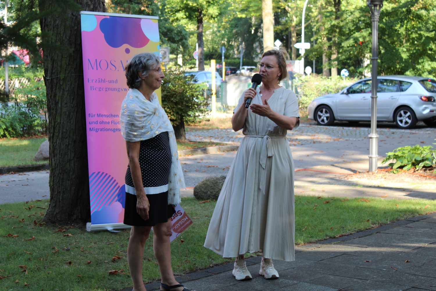 20. August 2024: Stefanie Müller (am Mikrofon), Leiterin des Kommunikationszentrums am Ostpreußendamm, begrüßt Dr. Rita Zobel, Projektleiterin der Mosaik Erzähl- und Begegnungswerkstatt