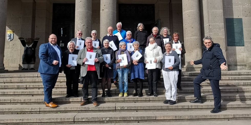 Eine Gruppe Menschen steht zusammen auf der Vortreppe von einem großen Gebäude. Die Menschen in der Mitte halten Urkunden in der Hand.