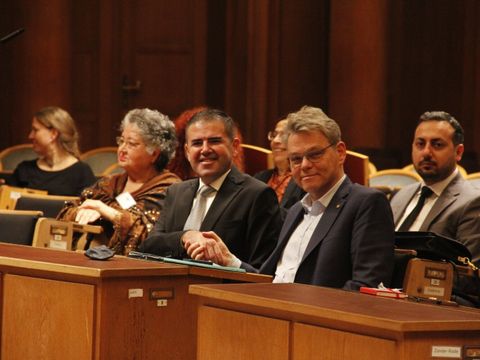 Bildvergrößerung: Zwei Männer sitzen nebeneinander und schütteln sich die Hände.