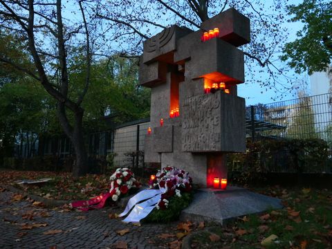 Bildvergrößerung: Ein Mahnmal wird im Dunkeln von vielen Kerzen erleuchtet. Vor dem Mahnmal liegen zwei große Kränze.