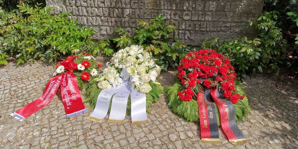 Drei Blumenkränze vor einem Gedenkstein.