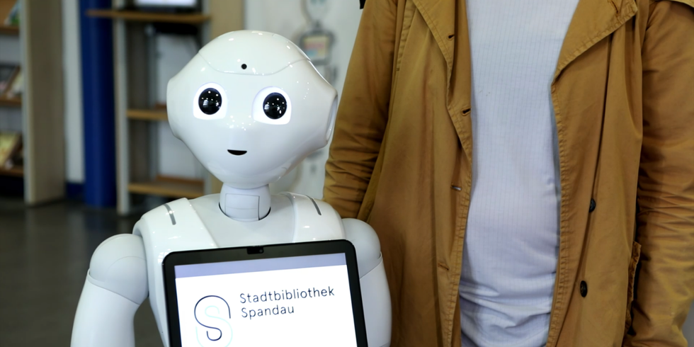 Ein Roboter mit einem Tablet auf der Brust mit der Aufschrift "Stadtbibliothek Spandau"