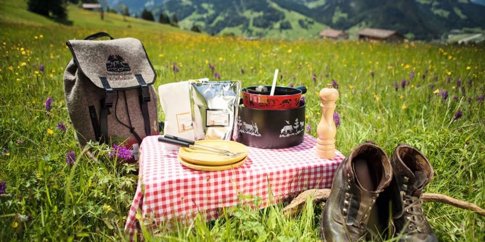 Gstaad Schoenried Fondue-Caquelon auf einem Tisch in Schlittmoos auf einer Wiese stehend mit Rucksack und Wanderschuhen 