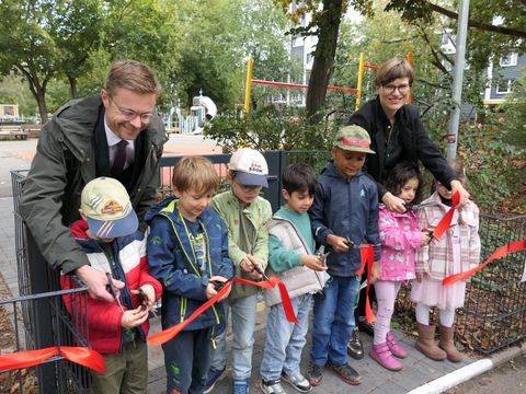 Christian Petermann und Annika Gerold durchschneiden mit Kindern das rote Band am Spielplatz Krautstraße