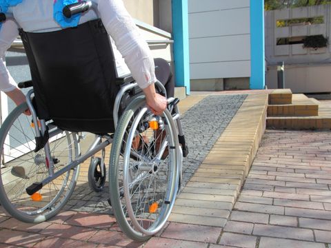 Person im Rollstuhl an einer rollstuhlgerechten Rampe, die zu einer Tür führt