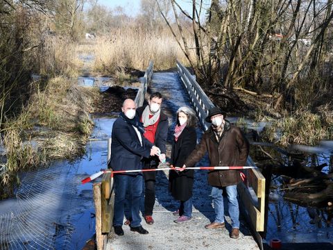 Bildvergrößerung: abgebildete Personen auf dem neuen Steg beim gemeinsamen Durchschneiden des Einweihungsbandes mit Masken: v. l. n. r.: Bezirksstadtrat Frank Bewig, Stefan Pasch (Fachbereichsleiter Grünflächen) Anja Sorges (Leiterin des Umwelt- und Naturschutzamtes) und Henning Molz (Umwelt- und Naturschutzamt, Bezirksamt Spandau)