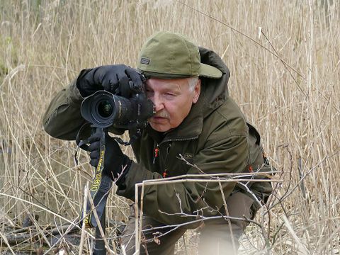 Naturfotograf Klaus Weber in Tarnkleidung mit Kamera und Stativ in der Natur 