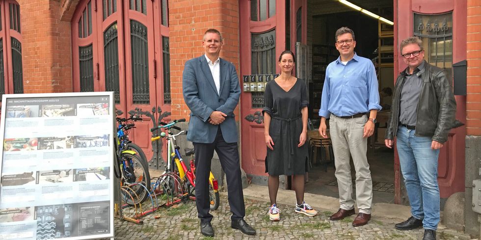 Vier Personen stehen nebeneinander vor dem Eingang in ein altes Backsteingebäude.