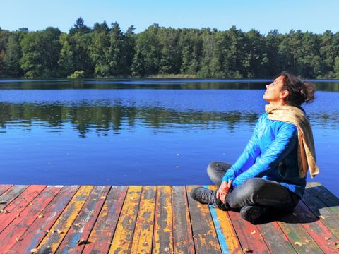 Frau sitzt auf dem Steg am See und genießt die Sonne