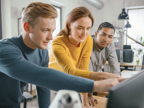 Eine Frau sieht mit zwei Kollegen auf den Monitor und bespricht Sachverhalte