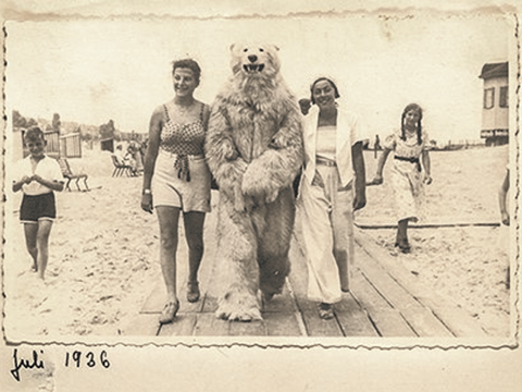 Bildvergrößerung: Zwei Frauen stehen auf einem Strand neben einer Person in einem Bären-Kostüm.