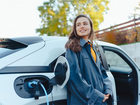 Frau lehnt an ihrem Elektroauto während es lädt