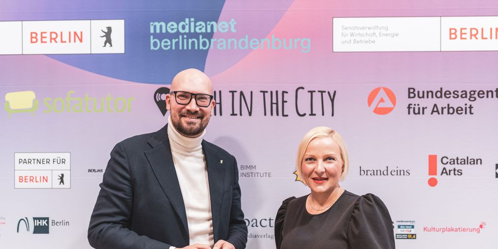 Staatssekretär Michael Biel und Jeannine Koch, Vorstandsvorsitzende von medianet berlinbrandenburg e.V. vor der Medienwand im ehemaligen Kino Colosseum.