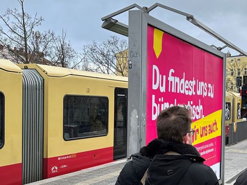 S-Bahn steht hinter Kampagnenplakat am S-Bahnhof.