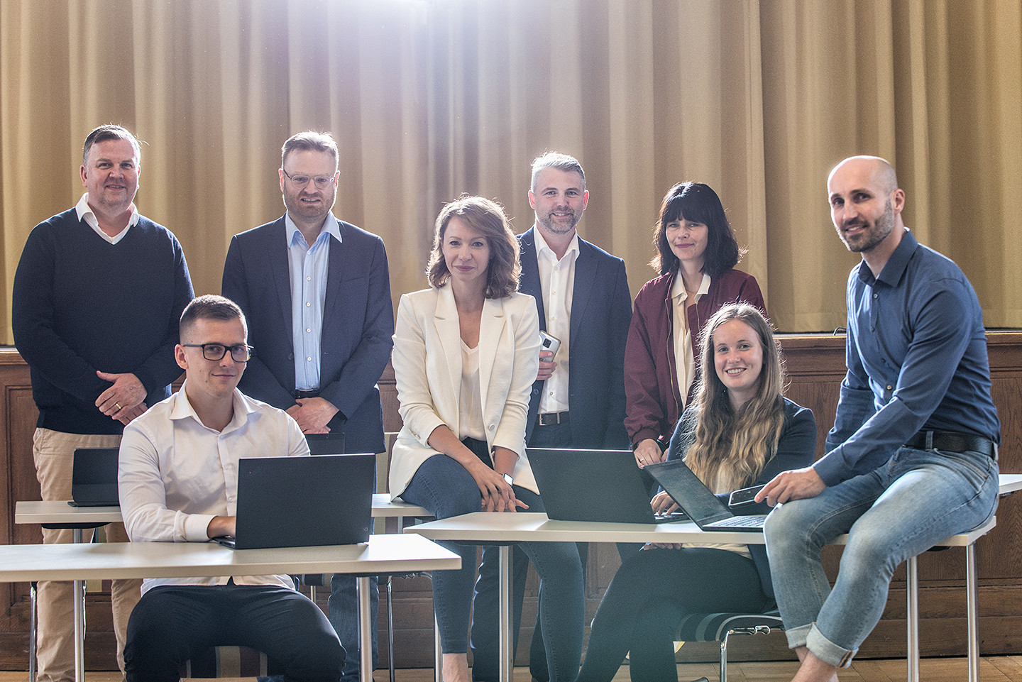 Gruppe von Menschen stehen um Schreibtische und lächeln in die Kamera