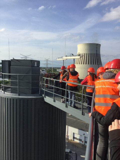 Männer mit roten Helmen und Warnwestern vor einem großen Kühlturm