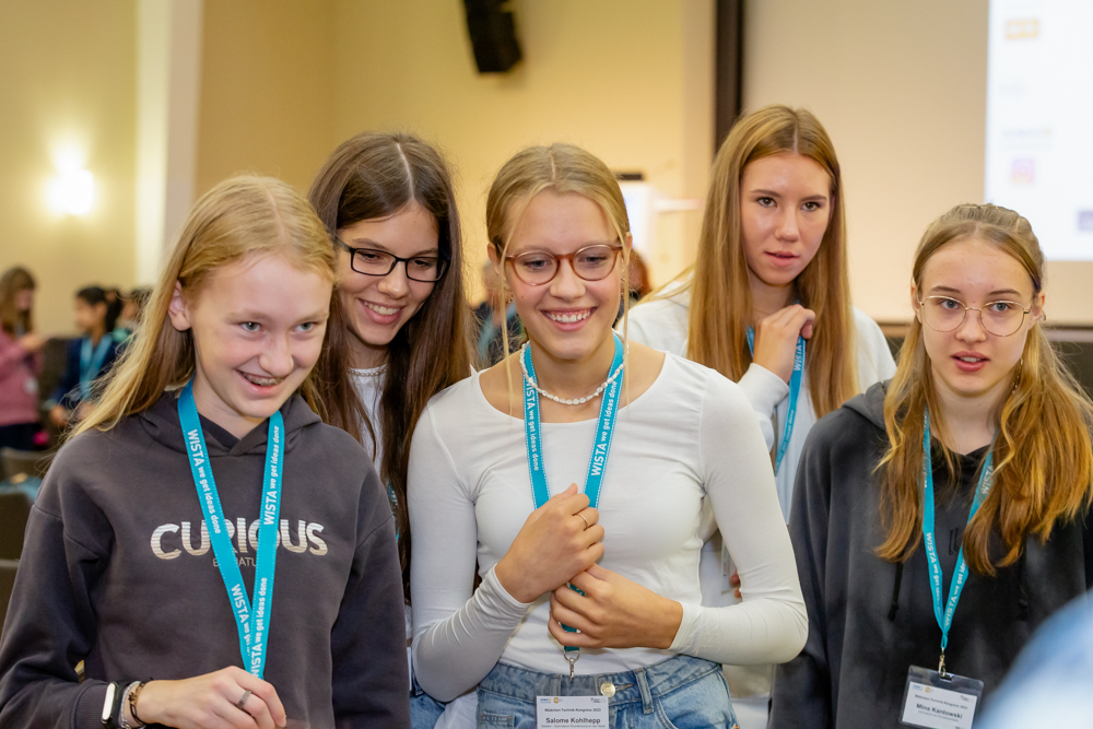 Füng junge Mädchen mit Akkreditierungsbändchen um den Hals schauen fröhlich irgendwo zu