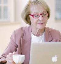 Seniorin sitzt vor einem Laptop mit einer Kaffetasse in der Hand