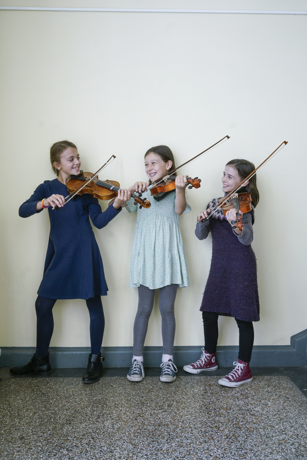 Drei glückliche Mädchen spielen zusammen Geige