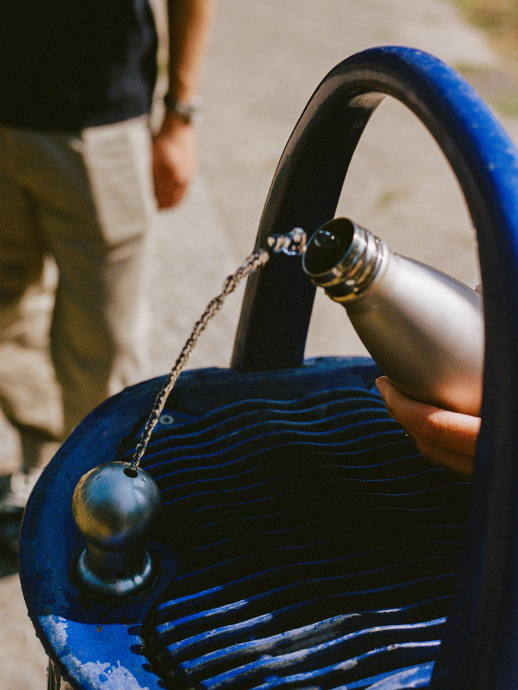 Eine Person füllt eine wiederverwendbare Trinkflasche an einem öffentlichen Trinkbrunnen auf. Der Brunnen steht für die Förderung von Mehrweg und den Zugang zu kostenlosem Trinkwasser im Kiez.