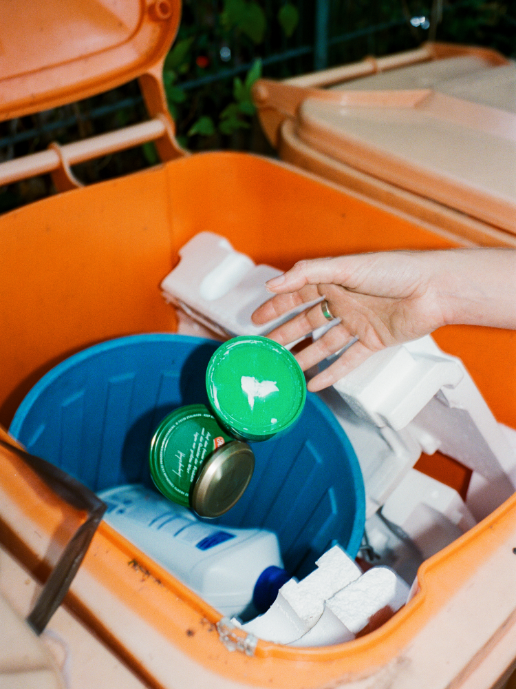 Hand wirft leere Dosen und Verpackungen in einen Wertstoffcontainer. Die Szene verdeutlicht verantwortungsvolle Abfalltrennung und Recyclingmöglichkeiten.