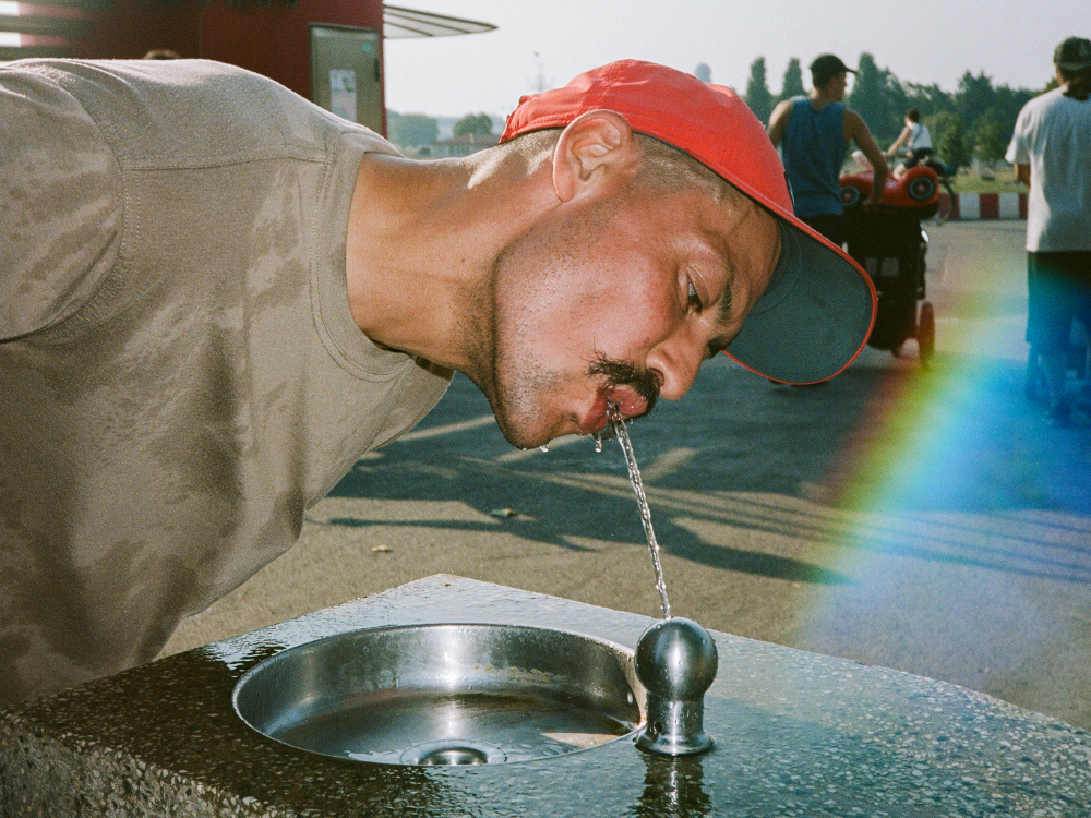 Ein Mann trinkt Wasser aus einem öffentlichen Trinkbrunnen. Die Aufnahme fördert den Zugang zu kostenlosem Trinkwasser und steht für nachhaltigen Konsum ohne Einwegplastik.