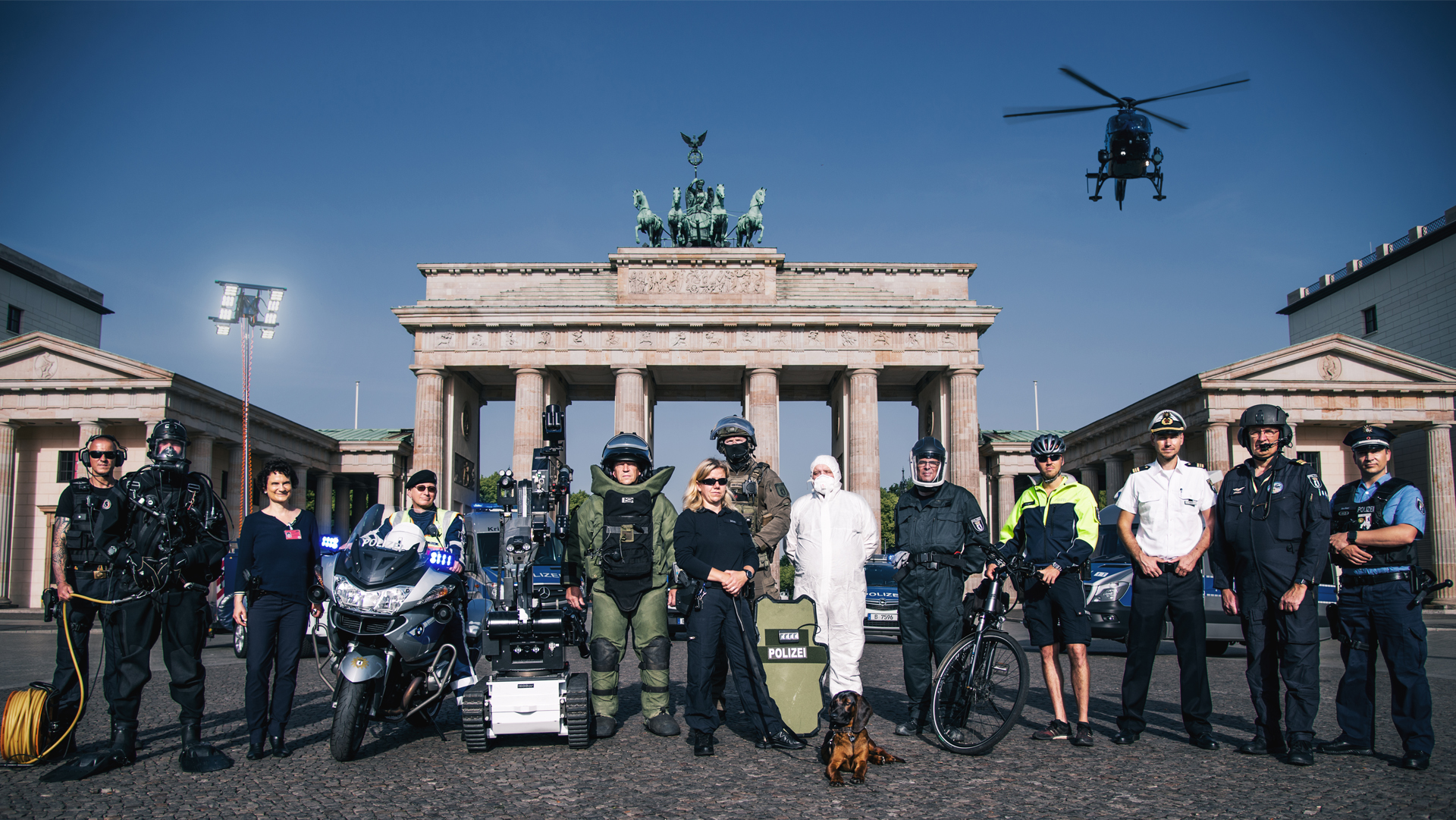 Polizisten in ihren Arbeitsbereichen vor dem Brandenburger Tor, Links oben Logo Kampagne 110 Prozent Berlin