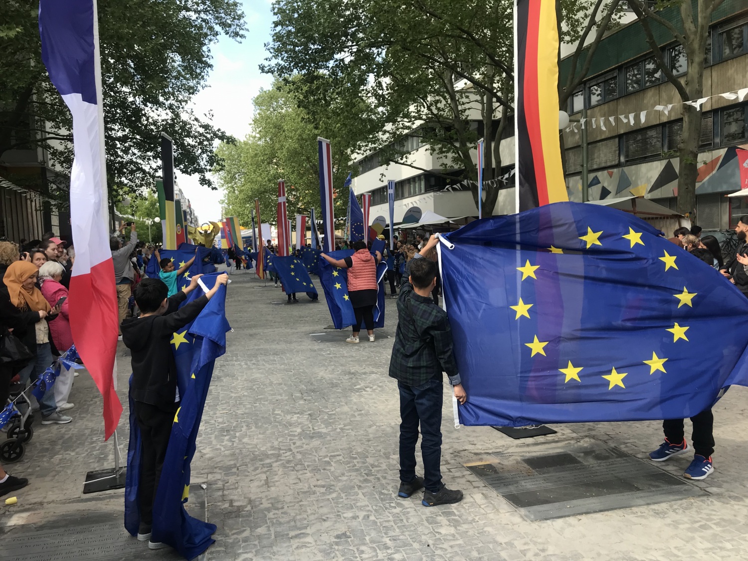 Kinder der Galilei Grundschule enthüllen die Zitateplatten und halten die Europafahnen hoch.