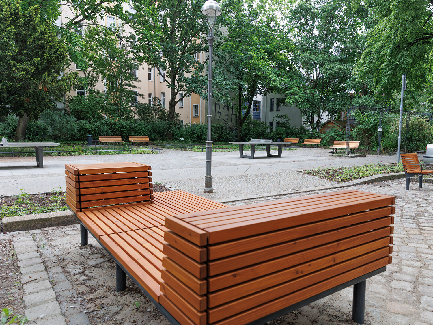 An beiden Zugängen zur Grünfläche stehen verschiedene Sitzmöbel und stabile Picknicktische.