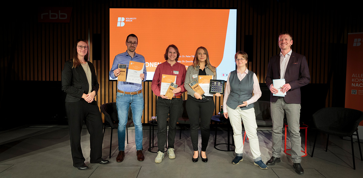 Gruppenfoto der Preisträger:innen mit Preisen auf der Bühne.