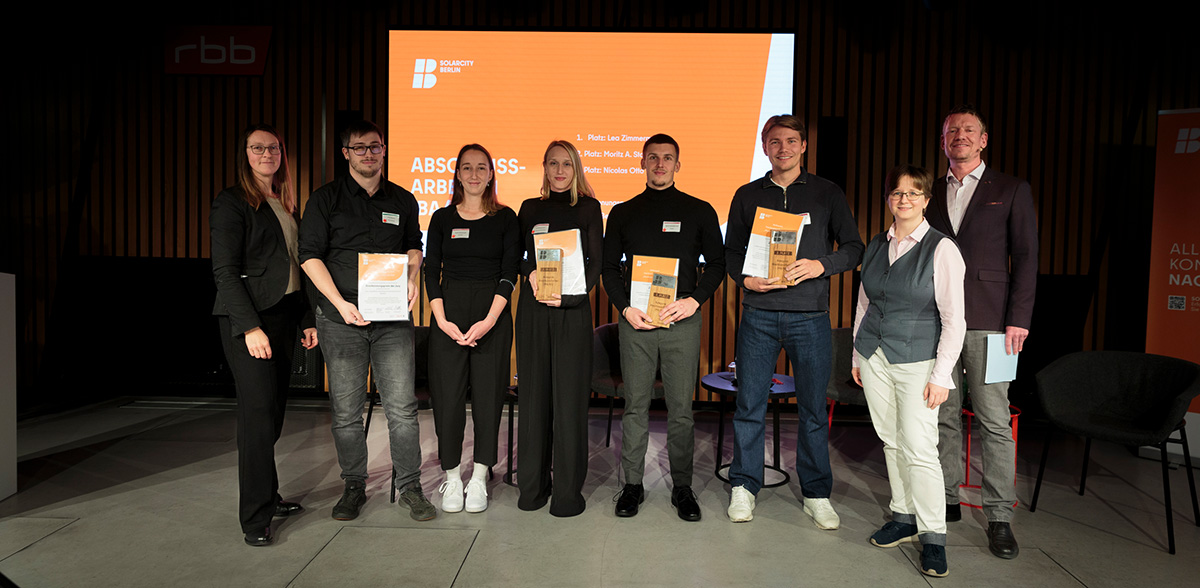 Gruppenfoto der Preisträger:innen der Abschlussarbeiten mit Preisen auf der Bühne.