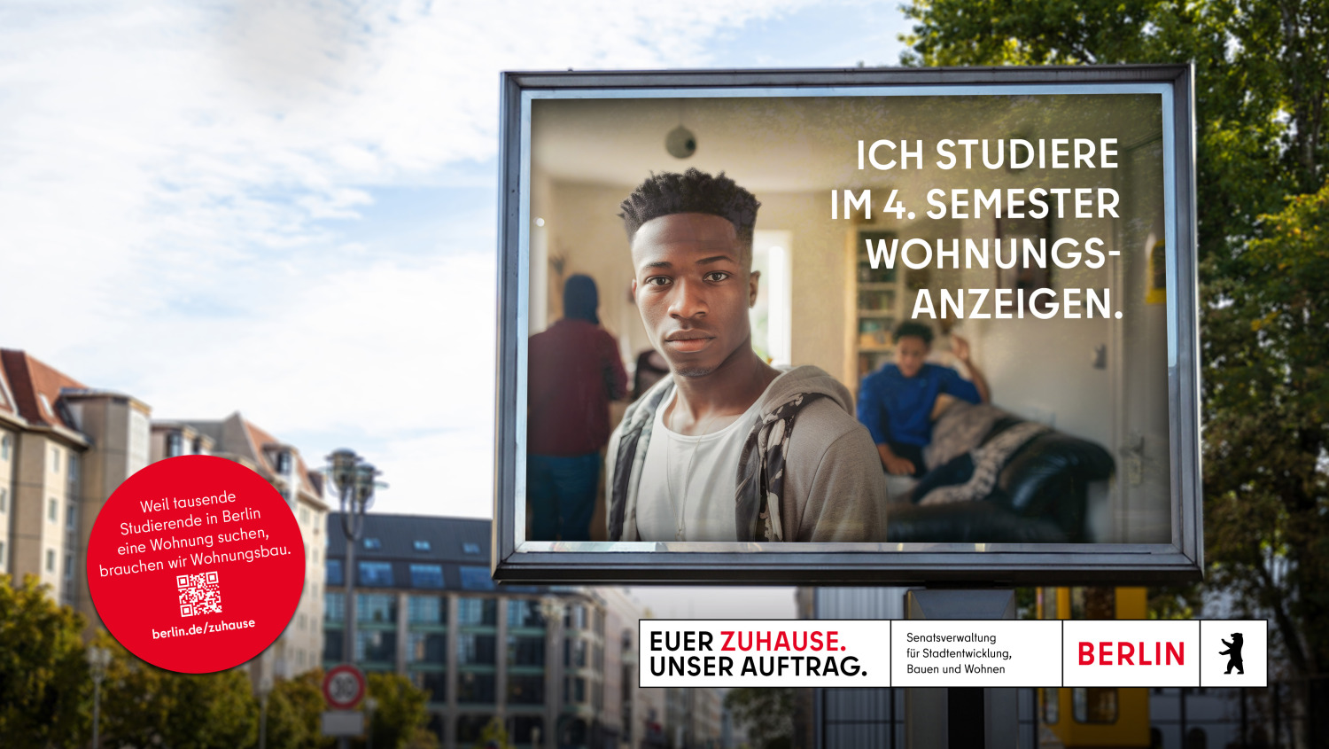 Auf einer Werbetafel in Berlin ist ein junger Mann abgebildet, der direkt in die Kamera blickt. Hinter ihm sind weitere Personen in einem Raum. Der Text auf der Tafel lautet: “ICH STUDIERE IM 4. SEMESTER WOHNUNGSANZEIGEN.” Im Hintergrund sieht man städtische Gebäude und Straßen.